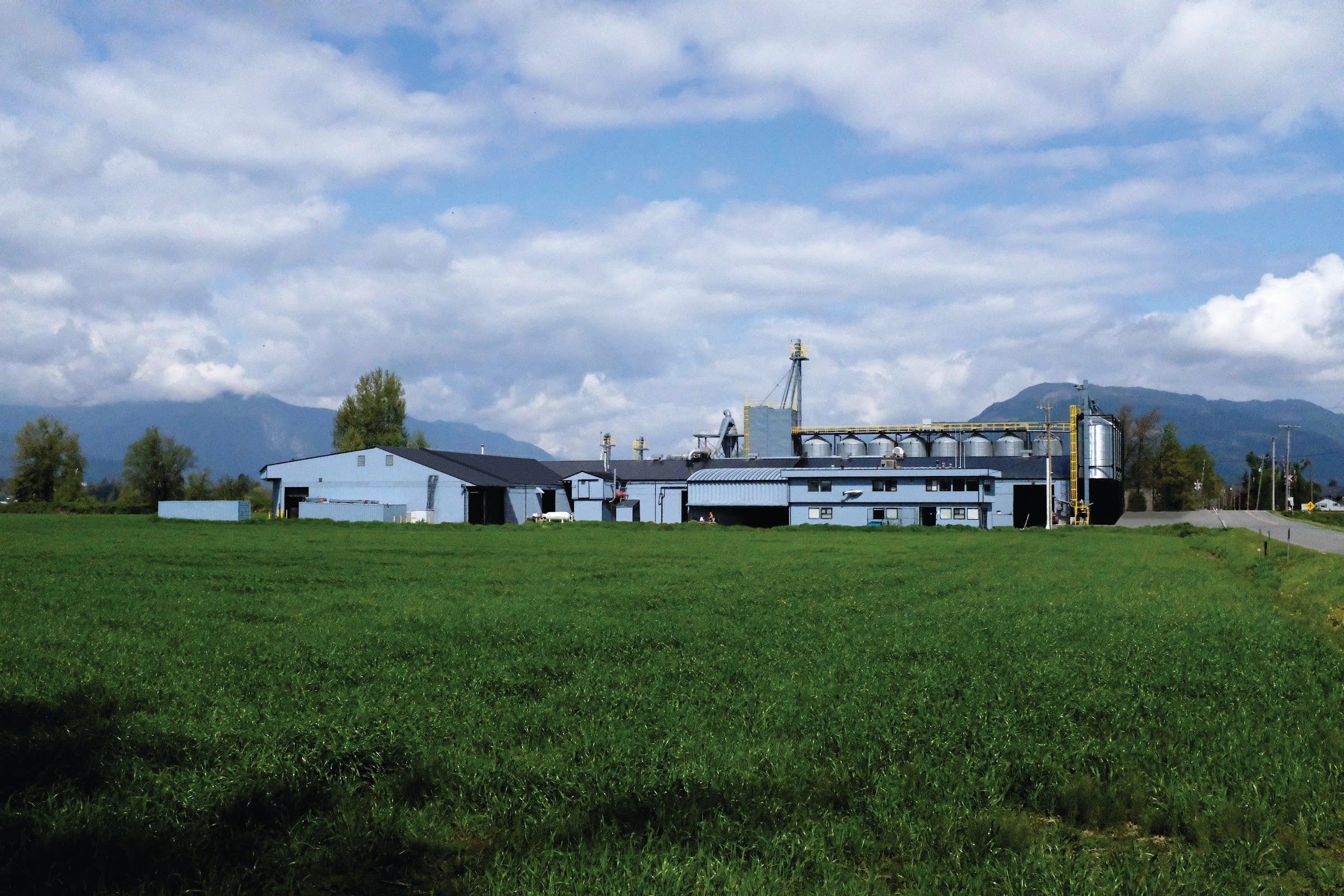 The FirstMate factory buildings in a green meadow, with the mountains of British Columbia behind them